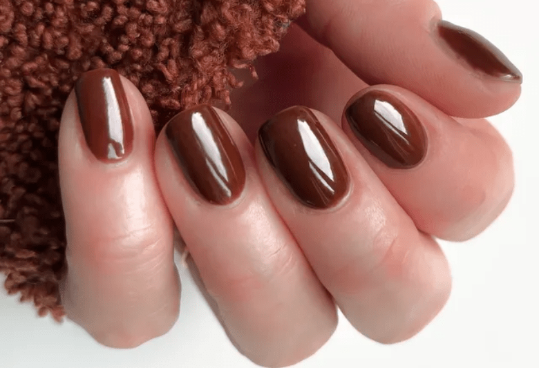 Close-up of a hand with brown painted nails against a background of brown textile.