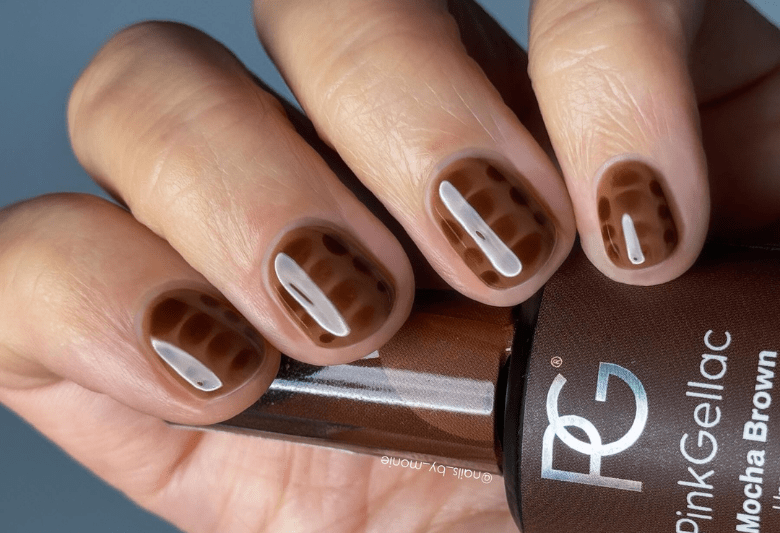 Close-up of a hand with nails painted in a shade of brown with a pattern that resembles an alligator skin, and a bottle of brown Pink Gellac nail polish that reads "Mocha Brown".