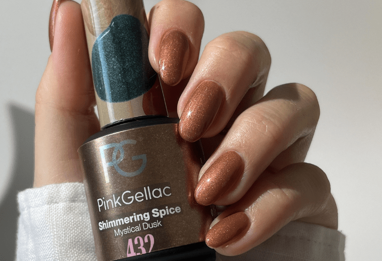Close-up of a hand with copper-colored nail polish, holding a bottle of "Pink Gellac Shimmering Spice".