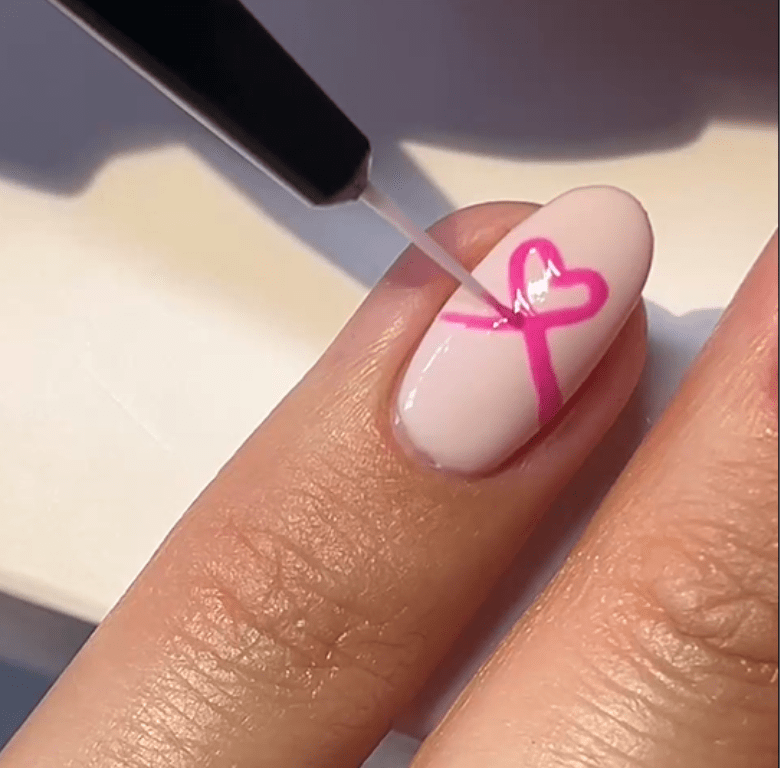 Nail is painted with a clear varnish over a pink ribbon design on a natural surface.