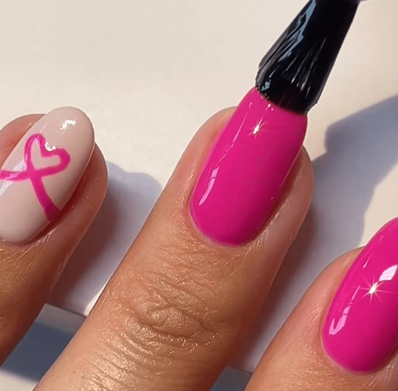 Nails are painted in bright pink color; Another nail has a white base with a pink heart and ribbon.