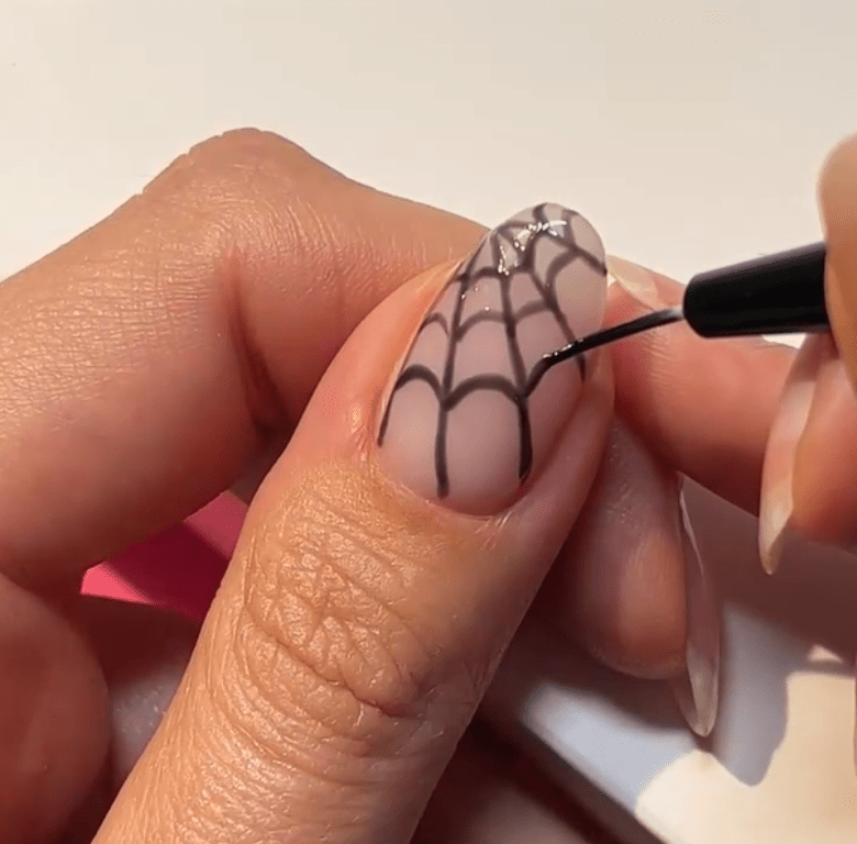 A hand painting a spider web pattern on a nail with a fine brush.