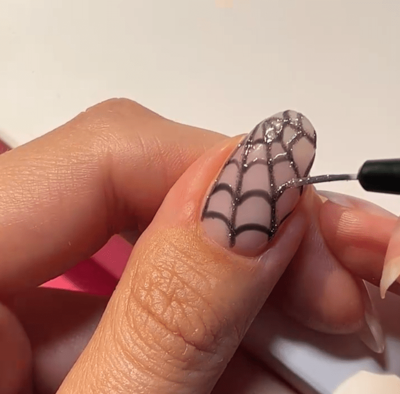 Person applies a design of a spider web to a fingernail with a brush.