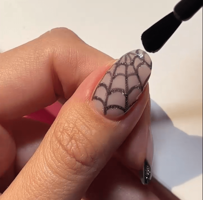Nail with black and white spider web nail art, lacquered with a brush.