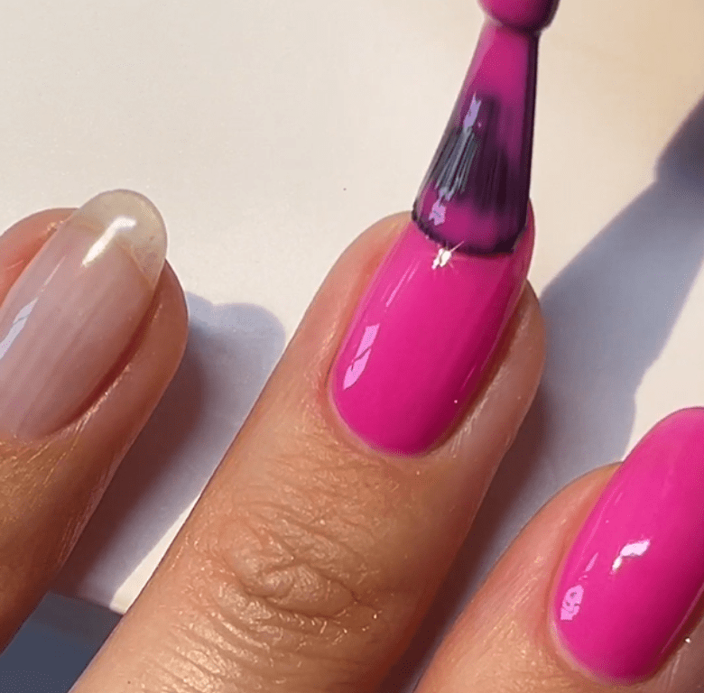 Person painting a nail with bright pink nail polish.