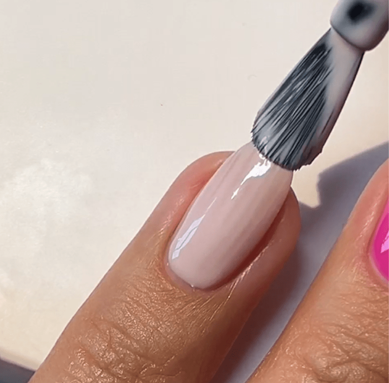 A nail is painted with light pink nail polish.