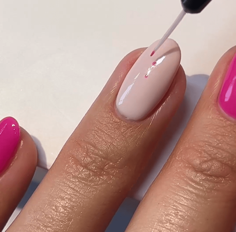A nail is painted with a light pink gel polish, while the surrounding nails are bright pink.