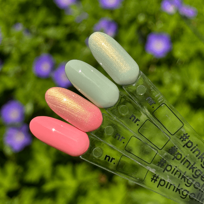 Four color samples of nail polish on plastic rods, in shades of pink, goldish, mint green and mother-of-pearl, against a background of vague purple flowers and green leaves.