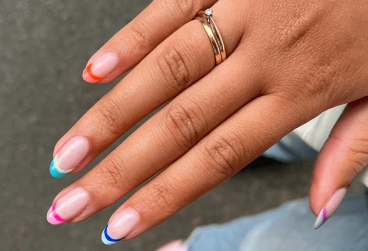 Hand with colored nails and a gold ring with a diamond.