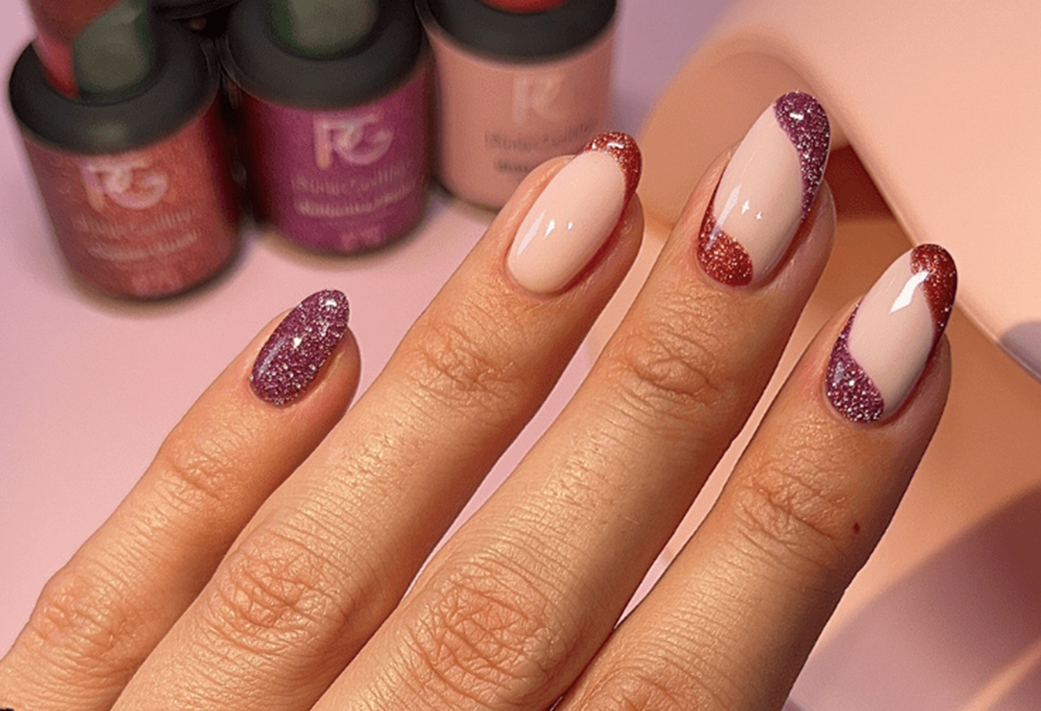 Nails with glittering pink and purple nail art, different designs and background bottles.