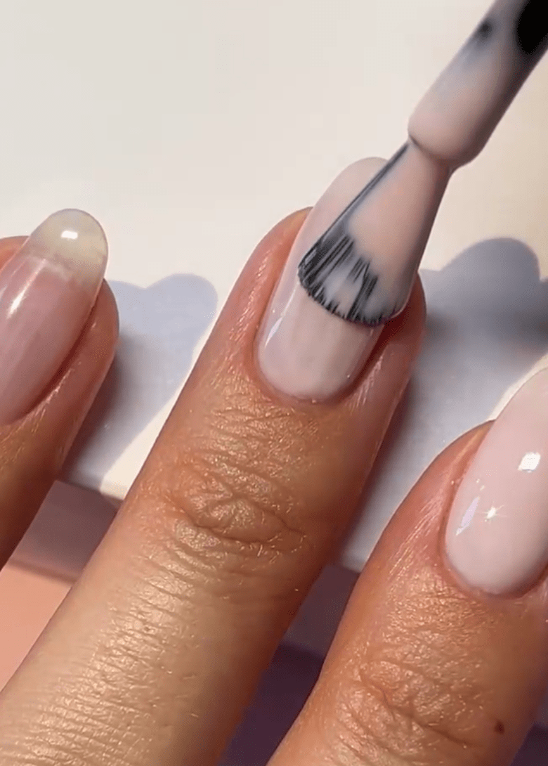 A brush applies a light pink nail polish to a fingernail.