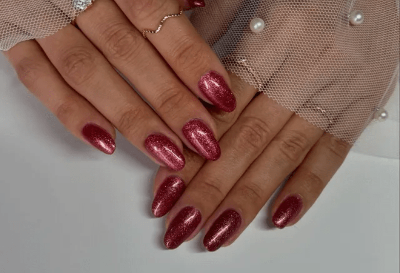 Two hands with shimmering, burgundy nail polish and a fine mesh with pearls in the background.