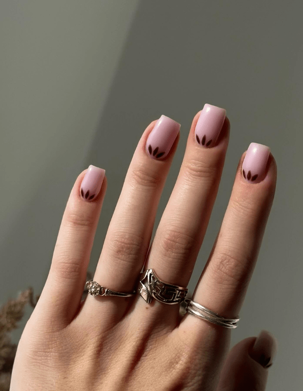 A hand with four silver rings and nails painted in pale pink with black leaf-like designs at the ends.