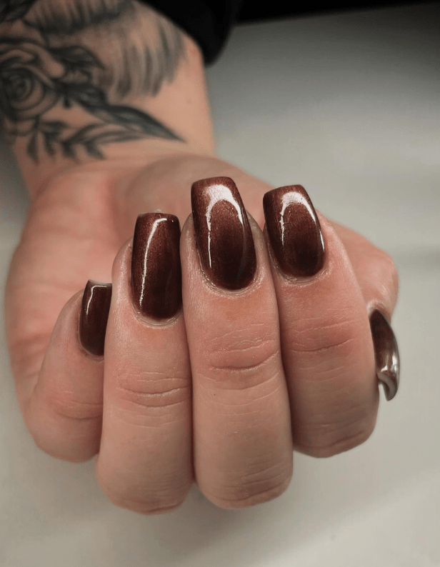 Close-up of a hand with brown, shiny gel nails and a tattoo of roses and leaves on the forearm.