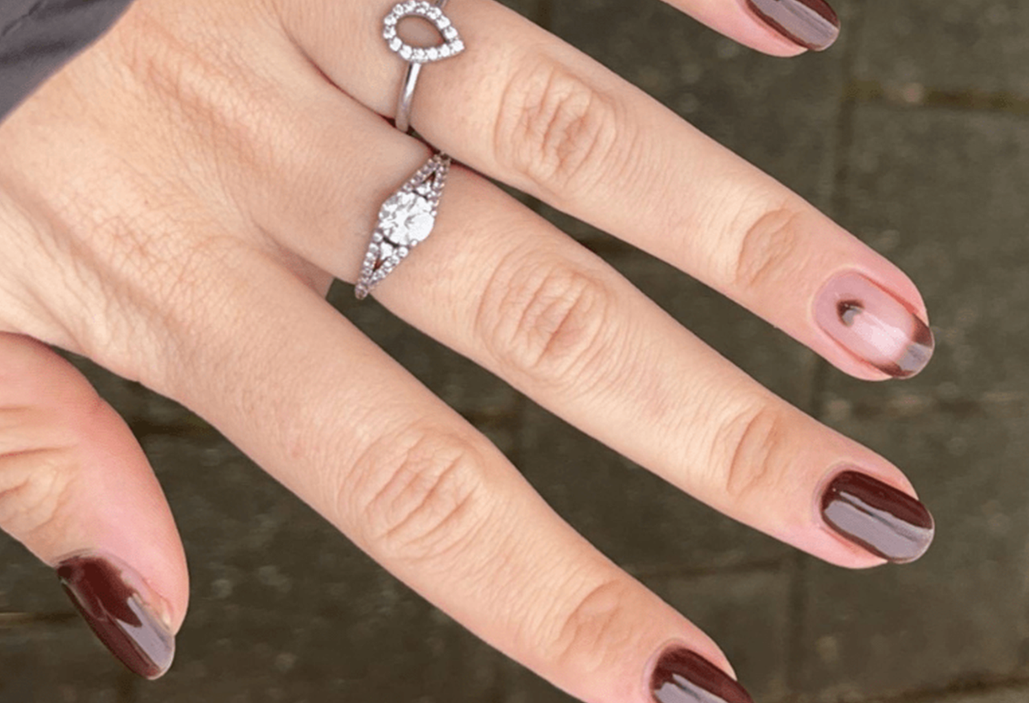 Close-up of a hand with dark red nail polish and two silver rings with gemstones.