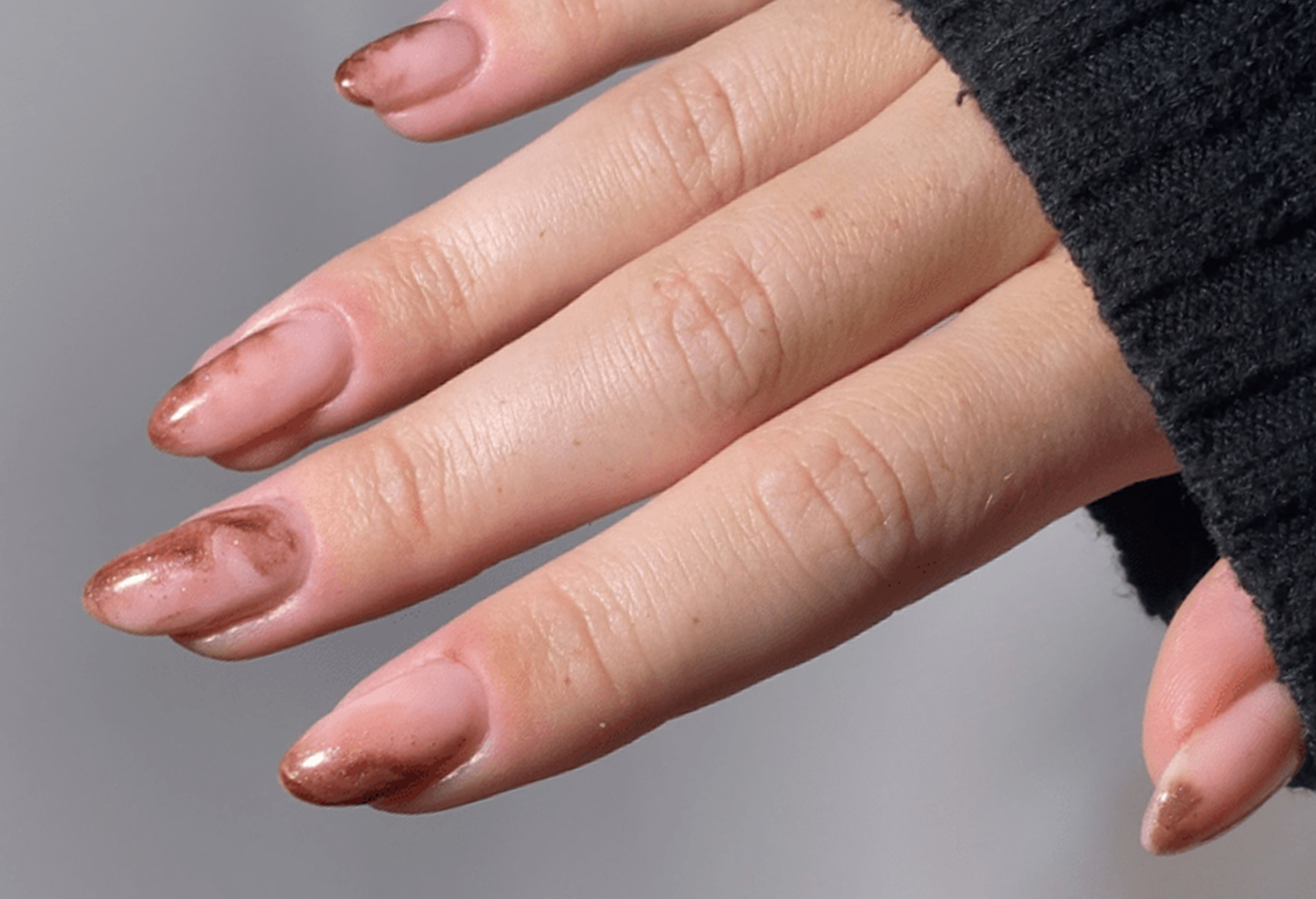 Close-up of a hand with long, painted nails, partly with a brown marble nail art, against a gray background.