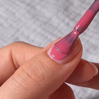 Hand painting a nail with pink nail polish.