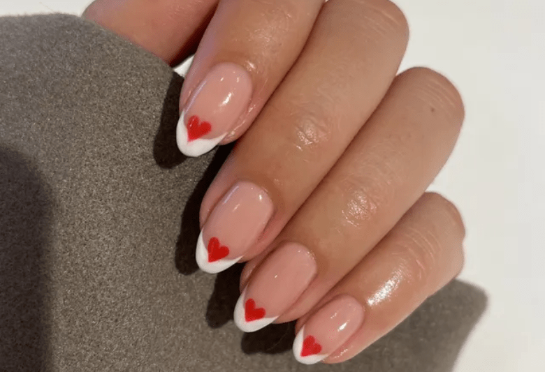 A hand with a manicure of pink nails with white tips and red hearts on each nail.