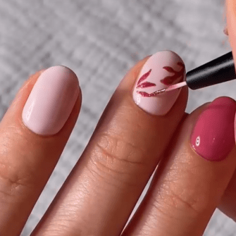 Nail art with pink base and hand-painted red leaves on the ring finger.