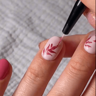 A hand gets a nail design of pink leaves on a light background with a fine brush.