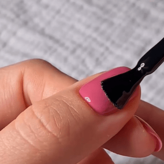 A hand showing a pink nail on which black nail polish is applied with a brush.