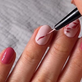 Close-up of a hand with someone applying pink nail art designs to light pink painted nails with a thin brush.