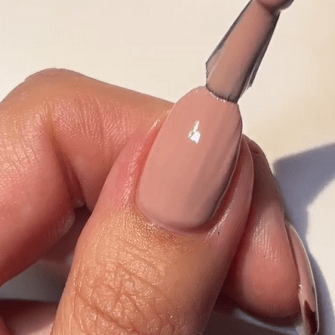 Hand with nail where a layer of nude-colored nail polish is applied with a brush.