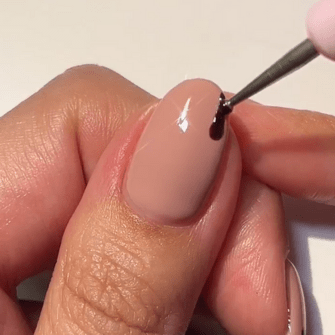 A close-up of a hand painting a nail with black nail polish.
