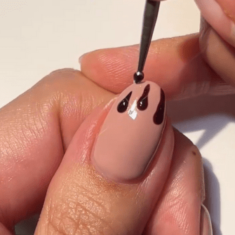A hand applying black paint to a nail with a nude base with a brush, creating a dripping effect.
