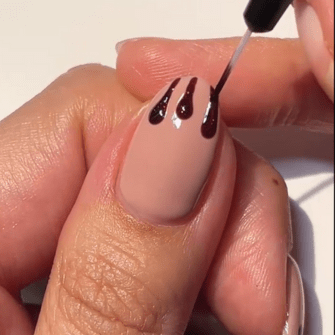 Nude colored nail is decorated with brown nail polish drop pattern.