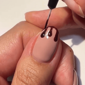 A hand that has a soft beige nail is decorated with dark brown nail polish in a dripping design.