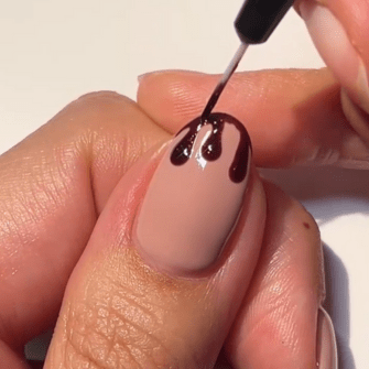 A hand with one©©finger whose nail is painted with a dark brown, dripping nail polish on a light pink base.