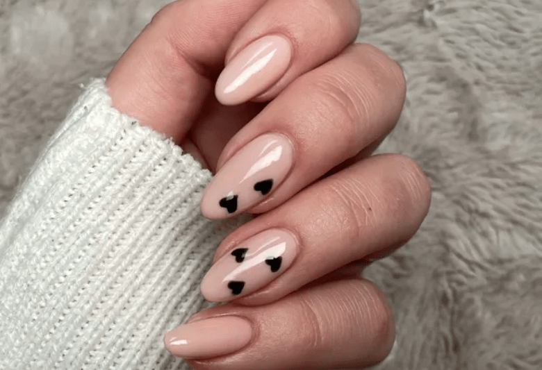 Hand with light pink manicure and black hearts on the middle and ring fingers, against a fluffy background.