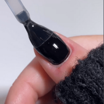 Close-up of a nail on which a black nail polish is applied with a brush.