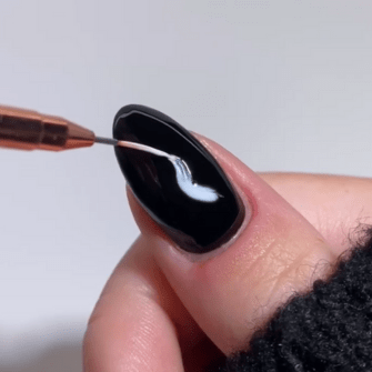 A nail is painted black with a thin brush that applies a white line.