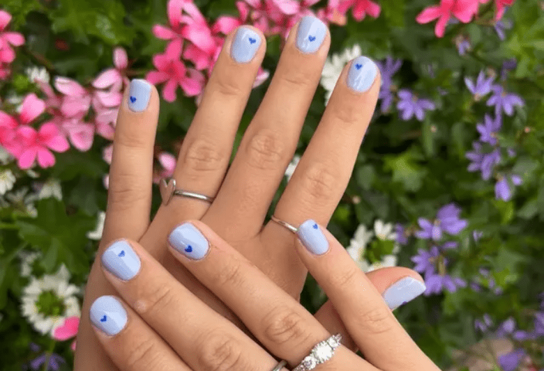 Hands with light blue nails and small hearts, against a background of colorful flowers.
