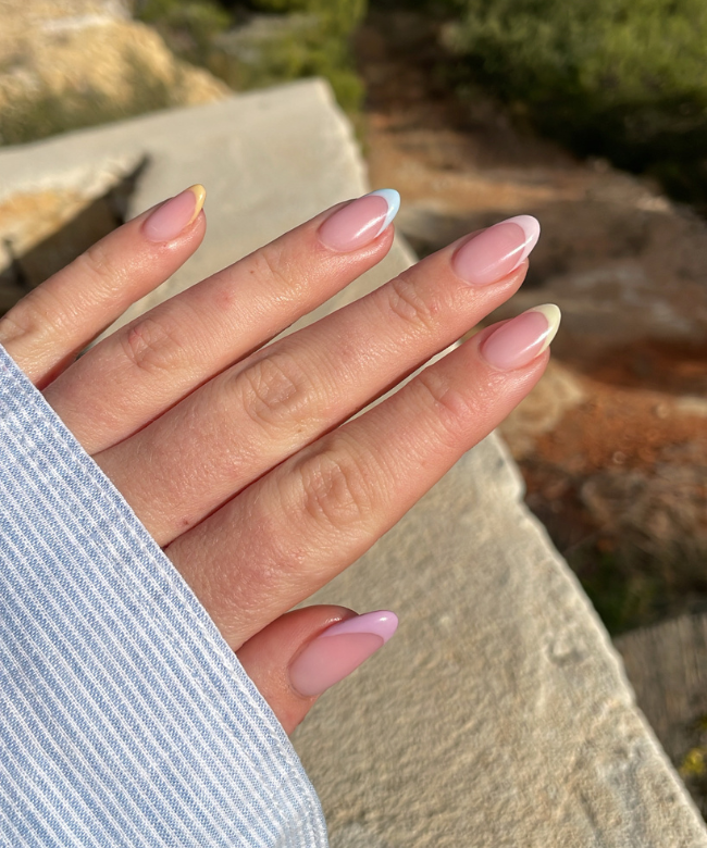Close-up of a hand with pastel colored nails on a sunny outdoor scene.