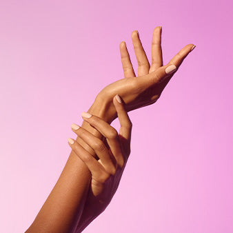 Two hands with manicured nails in an elegant pose against a pink background.