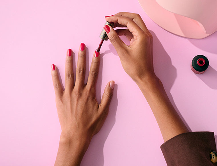 A hand applying red nail polish to another hand