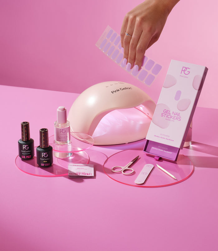 Nail care set with gel stickers, UV lamp, nail polish, scissors and file on pink background. Hand with stickers.