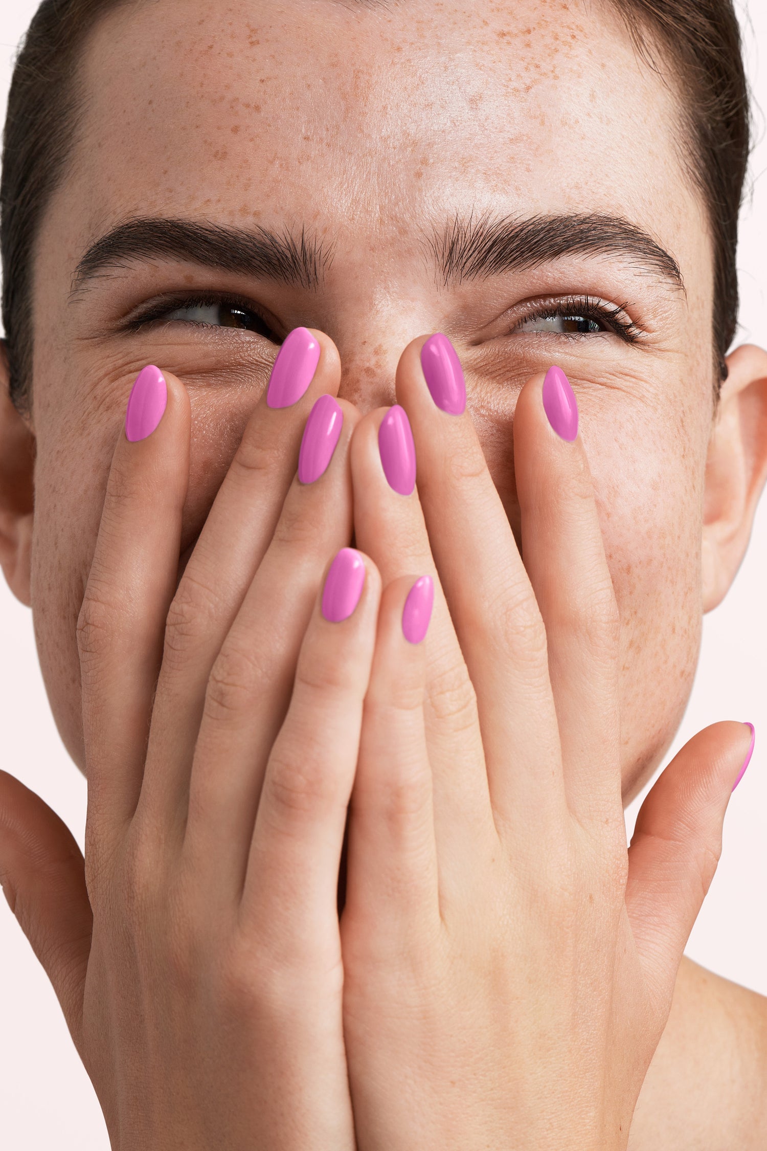 Person with a big smile smilingly covers her face with both hands, with pink painted nails.