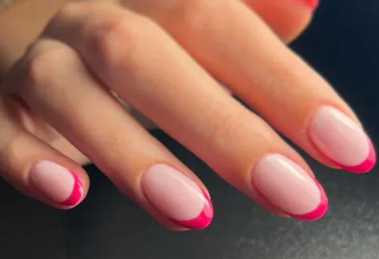 Hand with pink nails and fuchsia tips, styled in a modern manicure, against a dark background.