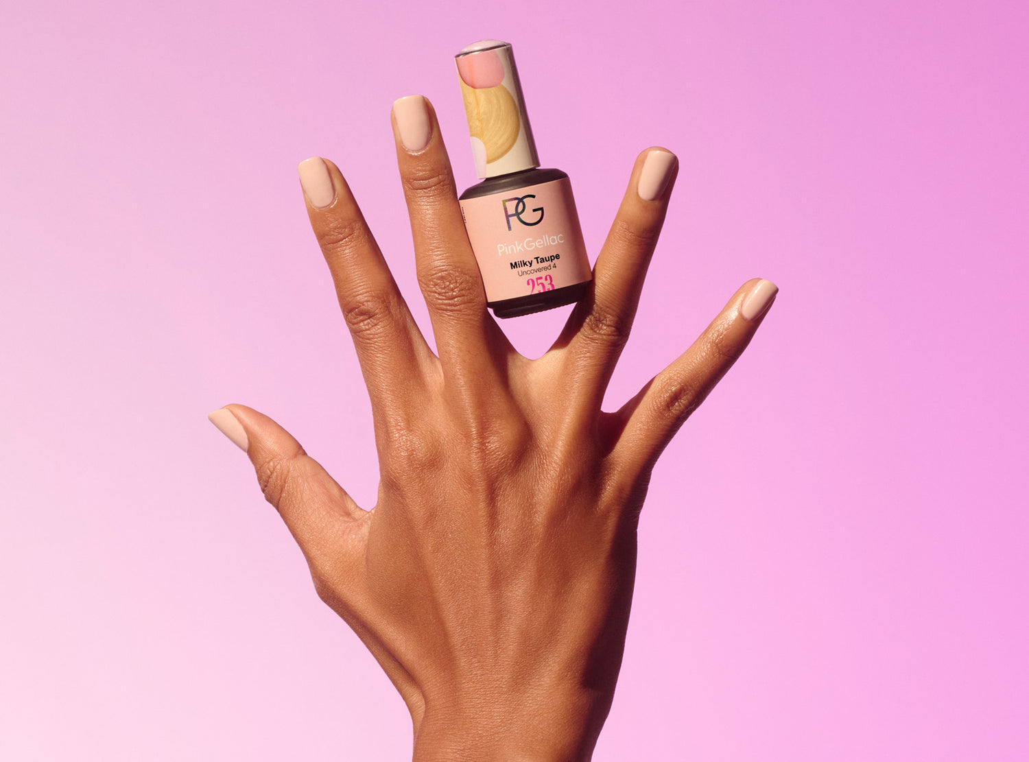 A hand with beautifully painted nails in a soft beige shade holds a bottle of Pink Gellac nail polish against a pink background.