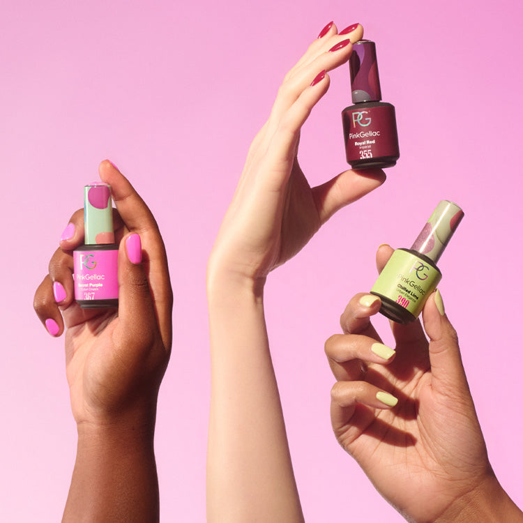 Three hands with different skin tones show nail polish bottles in pink, red and green against a pink background.