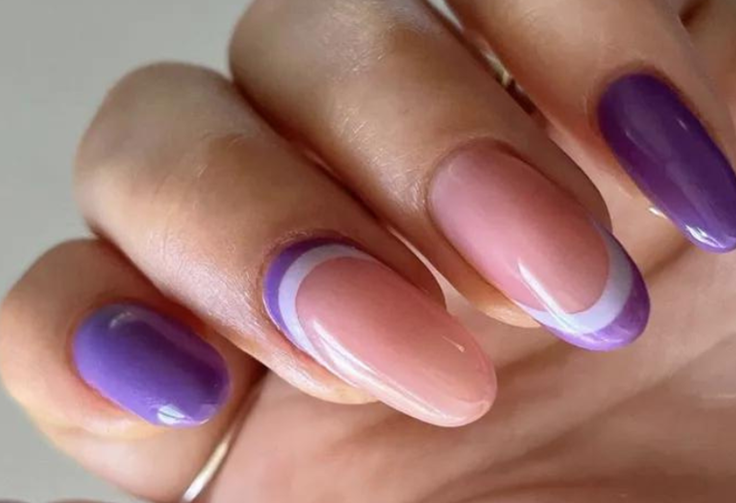 Hand with purple and nude nails, partly with a purple and white edge.