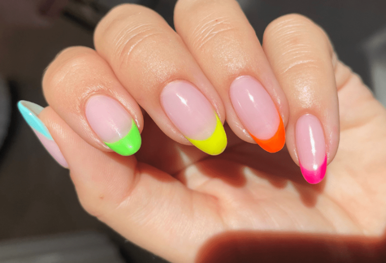 Hand with long, oval nails in bright blue, green, yellow, orange and pink neon french manicure.