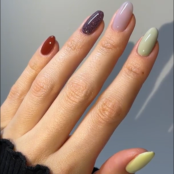 A hand with different nail polish colors, including dark red, shimmering purple, light pink, olive green and pale yellow.
