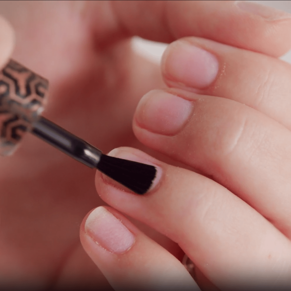 A person applies pink nail polish to a nail with a brush.