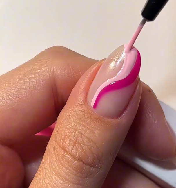 A hand with a nail is decorated with pink nail polish in a wavy pattern.