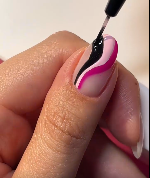 Close-up of a thumbnail with a colorful nail art design in pink, black and white, while applying a brush with topcoat.